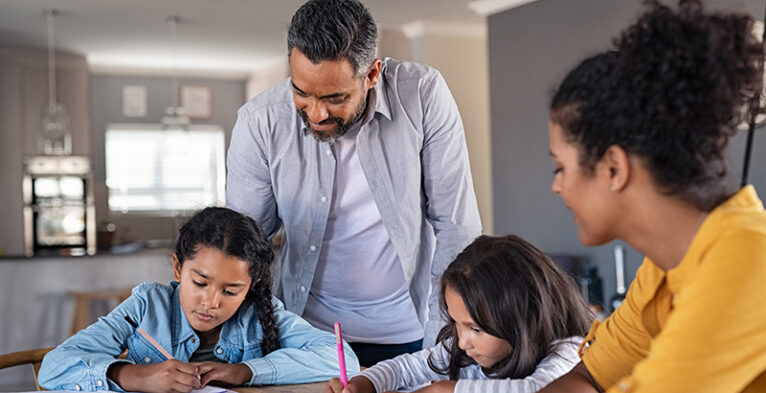 Indian parents helping children with their homework at home. Middle eastern father and african mother helping daughters studying at home. Little girls completing their exercises with the help of dad and mom, homeschooling concept.